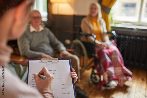 Close up of young woman writing on clipboard during therapy session at retirement home, copy space photo