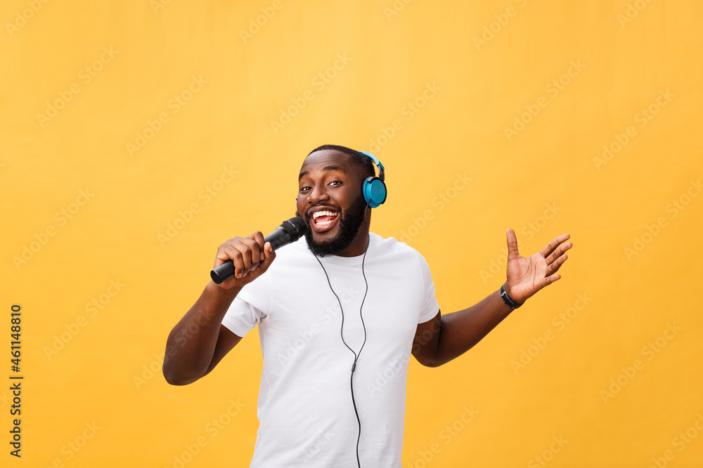 Portrait of cheerful positive chic handsome african man holding microphone  and having headphones on head listening music singing song enjoying weekend  vacation isolated on yellow background Stock Photo | Adobe Stock