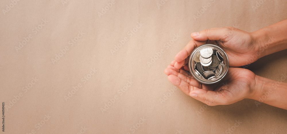 Woman hand holding money coin in glass jar on pink background, donation, saving, fundraising charity, family finance plan concept, superannuation, financial crisis concept, Top view. Woman hand holding money coin in glass jar on pink background, donation, saving, fundraising charity, family finance plan concept, superannuation, financial crisis concept, Top view.