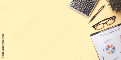 Office desk with analysis chart or graph, pen, eyeglass and calculator on yellow background. Top view with copy space, Working desk table concept. photo