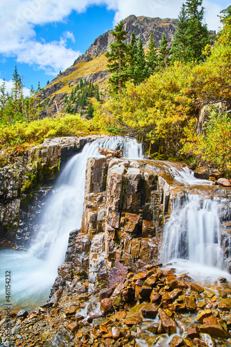 Waterfalls over chunks of rocks in the early fall with mountain in the background
