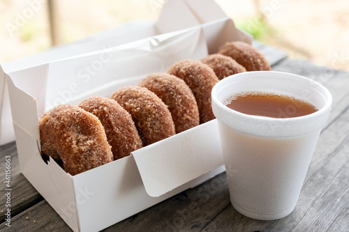 Photo Cup of apple cider and half dozen of cinnamon donuts on wooden table