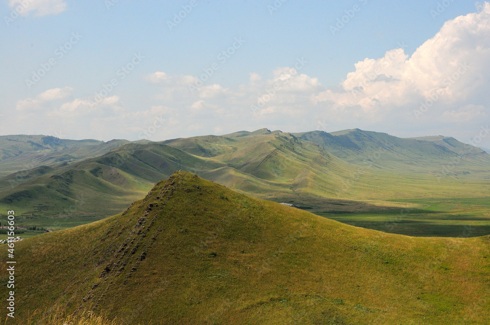 The ridge of a high mountain range passes through the steppe on a clear sunny day.