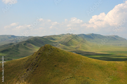 The ridge of a high mountain range passes through the steppe on a clear sunny day.