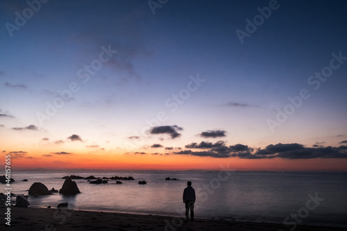 A man stands before the Kunisaki coast line in early morning. Sunrise sky over a rocky beach in early morning near Oita city, Japan. A seascape photo in Kunisaki japan 