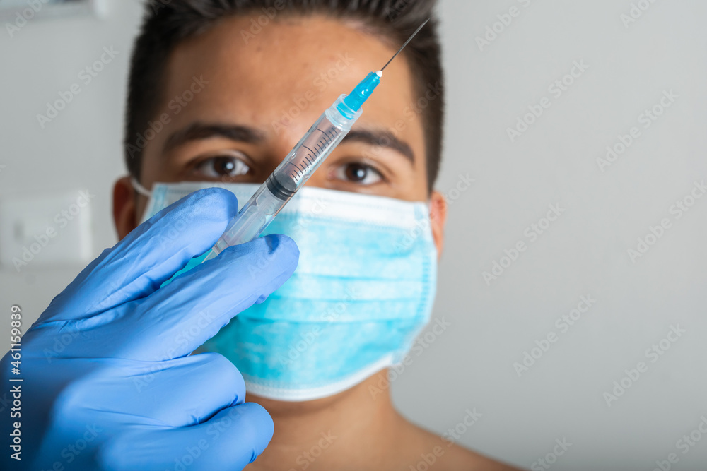 young latin male with surgical mask, shirtless, with syringe in hand prepared for vaccination, Rembrandt lighting (45° light) latex gloves (covid-19, influenza) pandemic and health concept young latin male with surgical mask, shirtless, with syringe in hand prepared for vaccination, Rembrandt lighting (45° light) latex gloves (covid-19, influenza) pandemic and health concept