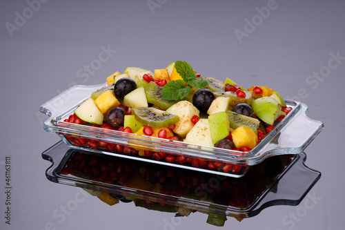 Mixed fruit salad arranged in a transparent rectangle tableware and garnished with mint leaf.