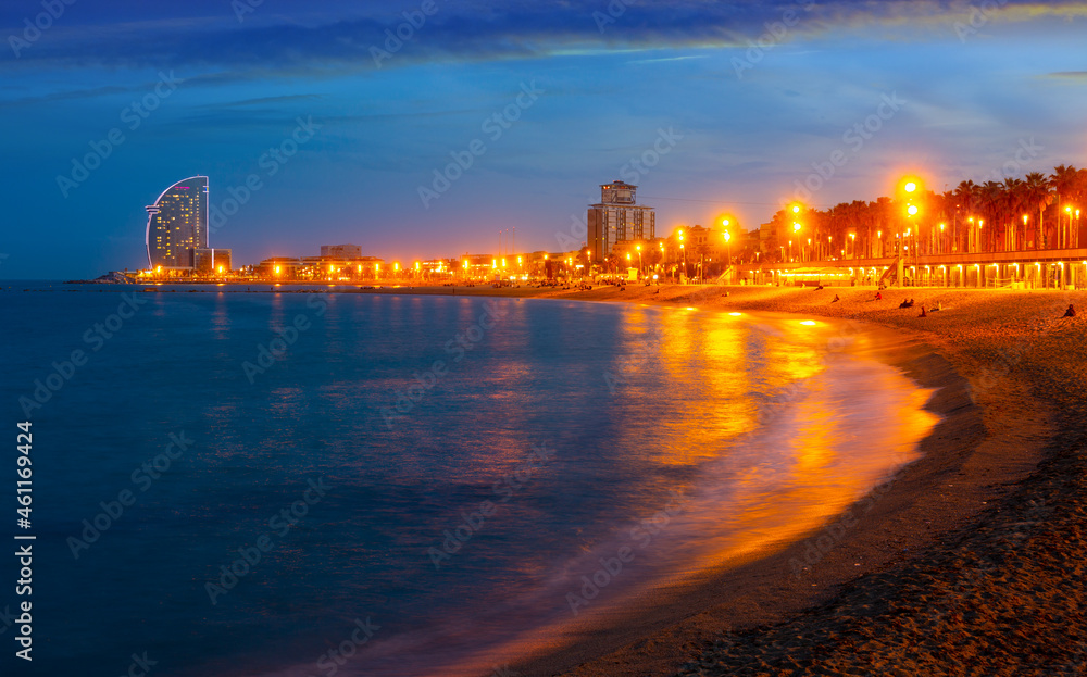 Illuminated Barceloneta beach on Mediterranean coastline overlooking luxury hotel W Barcelona on summer night, Barcelona, Spain