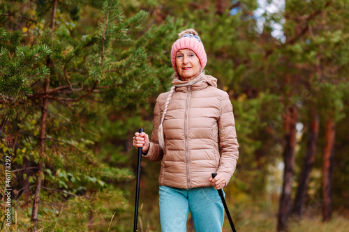 elderly sixty-year-old woman in sportswear is engaged in Nordic walking with sticks in the forest in the autumn