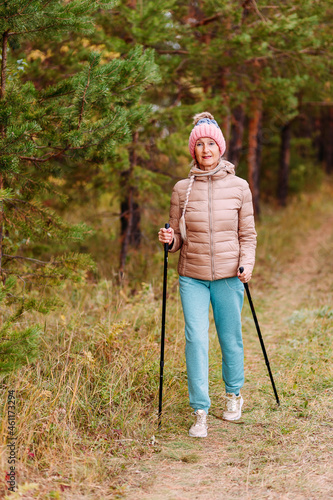 elderly sixty-year-old woman in sportswear is engaged in Nordic walking with sticks in the forest in the autumn