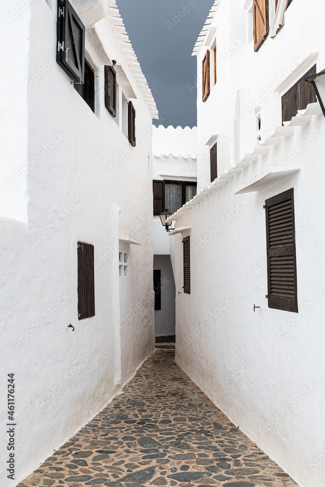 Narrow cobble stone street between white solid buildings in Menorca, Spain