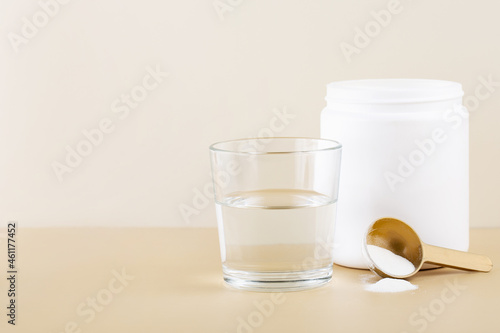 marine collagen in a white jar, a glass of water, beige background