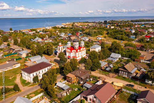 Scenic aerial view of Kozmodemyansk townscape on banks of Volga River overlooking red roof of ancient five-domed Orthodox Cathedral of Smolensk Mother of God in summer, Mari El, Russia