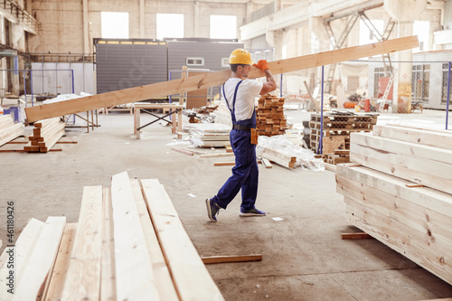 Male builder carrying wooden plank at construction site photo