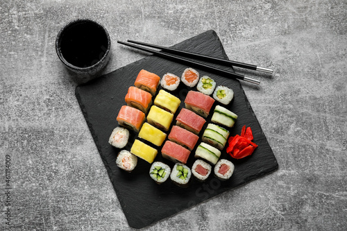 Set of delicious different sushi rolls, chopsticks and bowl with soy sauce on grunge background
