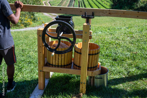 Young man turns crank on apple cider press with farm nature background photo