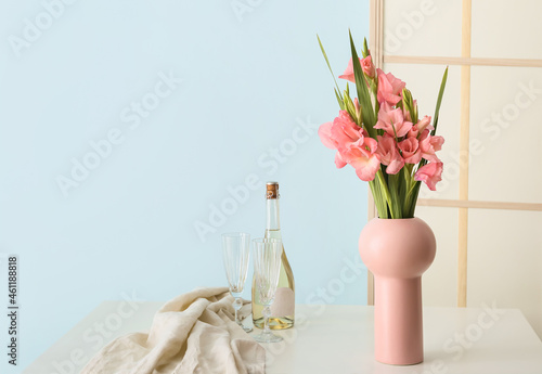 Vase with gladiolus flowers and bottle of champagne on table in room