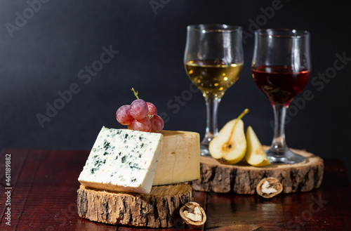 Wine, cheese, some grapes and pear on wooden plate on black background