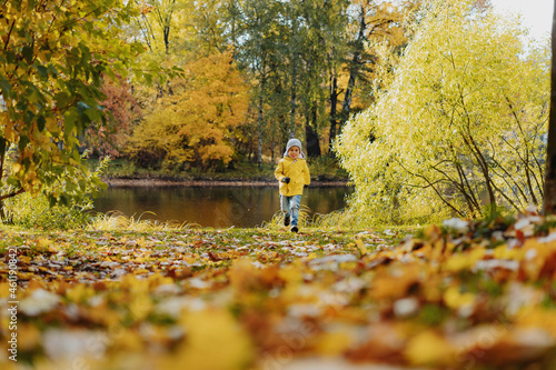 happy smiling little boy in yellow jacket run in autumn central park in Saint-petersburg, Russia on sunny october day