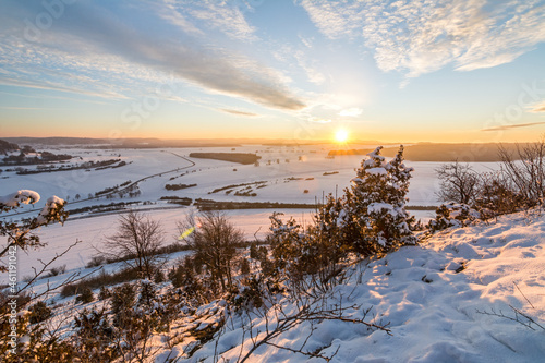 Scenic sunset over snowy winter landscape in the Swabian Alps with bushes and trees in the foreground