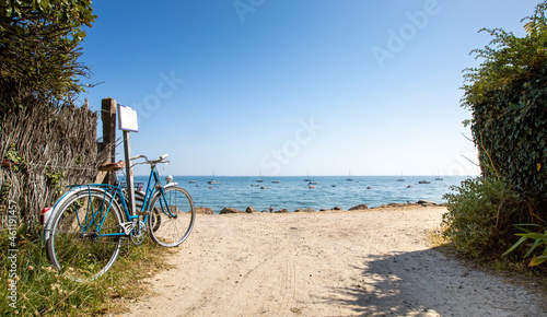 Vieux vélo bleu en bord de mer, sentier donnant sur la plage.