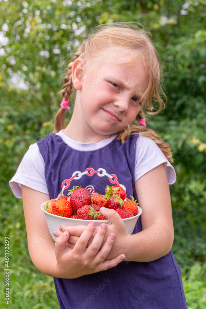 The girl holds a ripe juicy red fragrant strawberry in her hands. The girl holds a ripe juicy red fragrant strawberry in her hands.