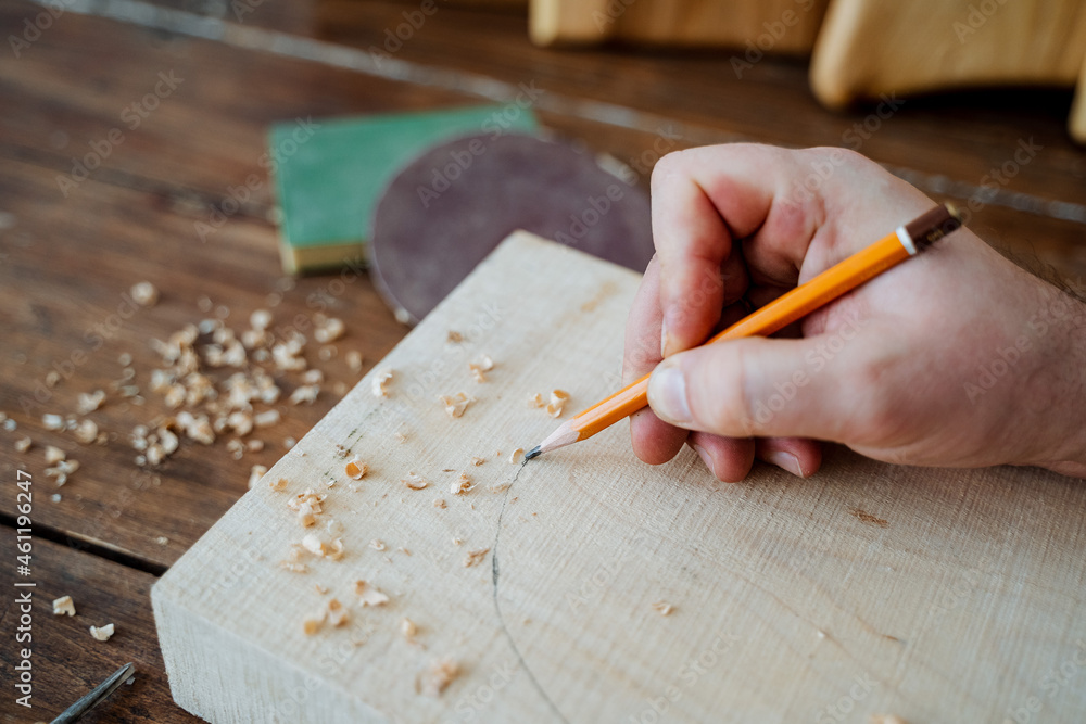 The carpenter draws with a pencil on the board. hand holds a pencil, carpentry workshop, sketch of the future product The carpenter draws with a pencil on the board. hand holds a pencil, carpentry workshop, sketch of the future product