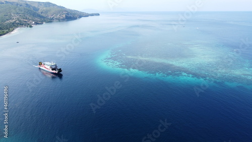 A passenger ferry leaving the stunning tropical Atauro Island with turquoise blue ocean and coral reef in Timor Leste, aerial view photo