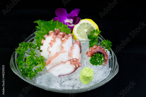 Octopus tentacles in a bowl over ice served with wasabi and oba leaves, lemon