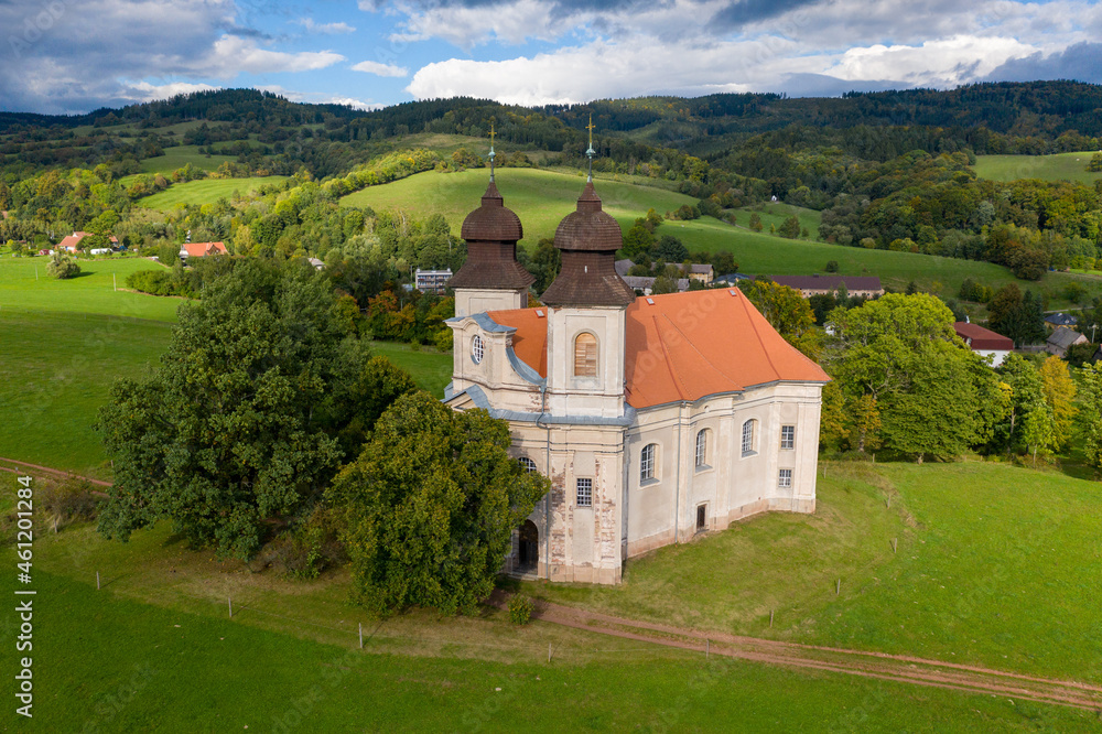 Fototapeta premium Church of St. Margaret from the 18th century near Šonov. Beautiful church chapel in middle of fields in czech countryside broumovsko region with hills of broumov walls on background. Aerial view 