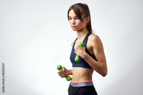 pretty woman with dumbbells in hand with workout exercises light background