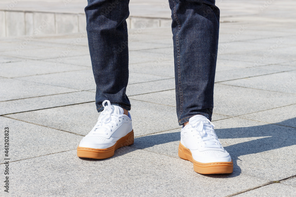 Male legs in jeans and white sneakers close-up on concrete background.