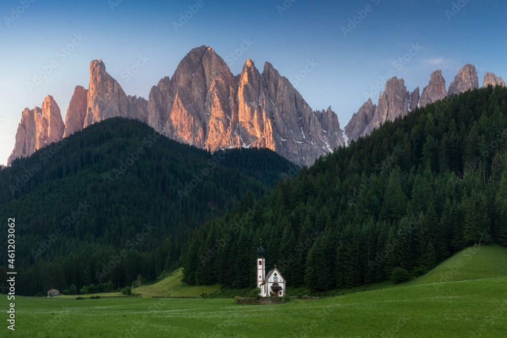 Sunrise of the St Johann Church, Santa Maddalena, Val Di Funes, Dolomites, Italy.
Furchetta and Sass Rigais mountain peaks in background. Blue sky during summer.