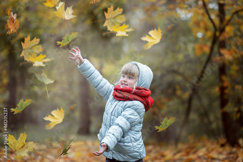 A girl walks in the park and throws up autumn leaves