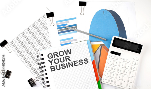 Text GROW YOUR BUSINESS on a notebook on the diagram and charts with calculator and pen