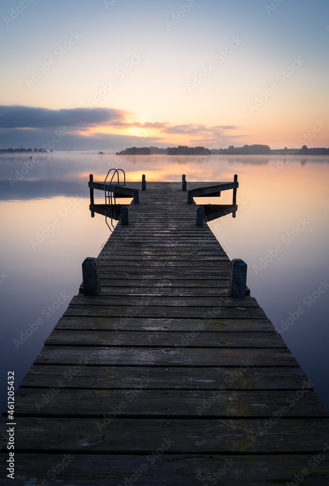 Fototapeta premium An empty jetty in a lake during a tranquil, foggy dawn.