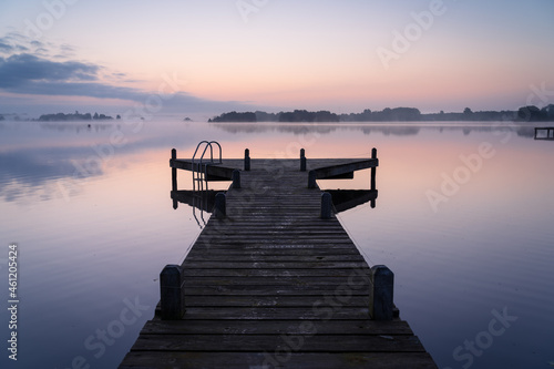 An empty jetty in a lake during a tranquil, foggy dawn.