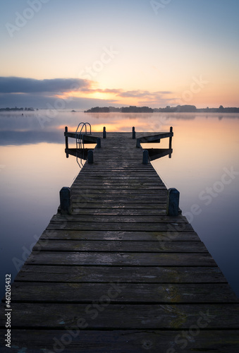 An empty jetty in a lake during a tranquil, foggy dawn.