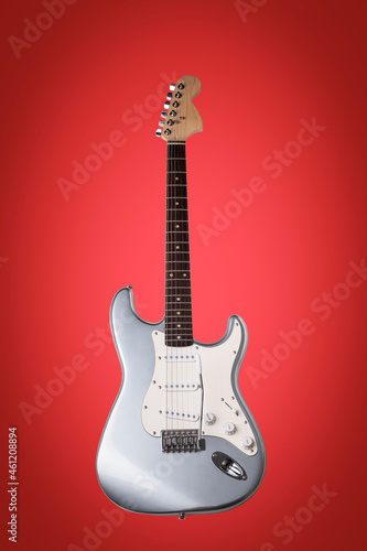 Silver electric guitar isolated on red background.