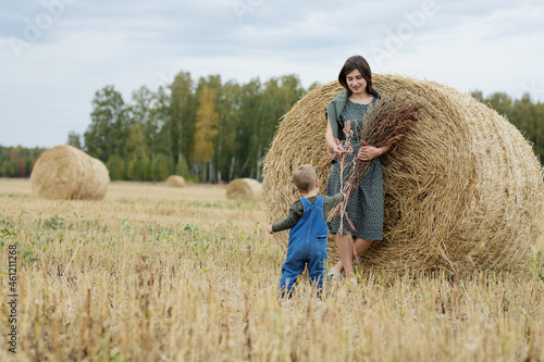 Beautiful  young mother and cute  son toddler are having fun on a haystack in the field 