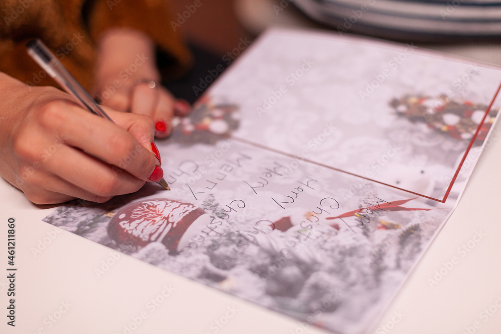 Closeup of girlfriend hands writing xmas greeting card for family during christmas holiday standing in xmas decorated kitchen. Happy family enjoying spending winter season together Closeup of girlfriend hands writing xmas greeting card for family during christmas holiday standing in xmas decorated kitchen. Happy family enjoying spending winter season together