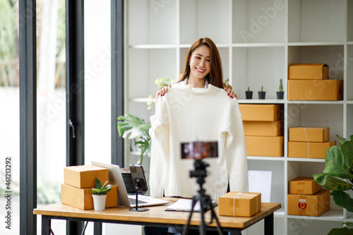 Young Asian women blogger showing clothes in front of the camera to recording vlog video live streaming at her shop. Network technology Business online influencer on social media concept.
