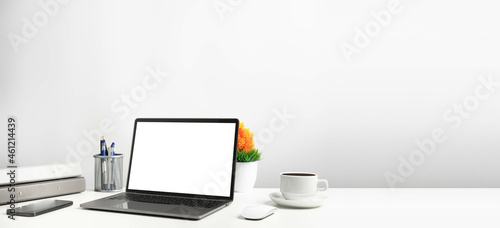 Blank white screen laptop on a white table in the office. Working concept using technology smartphones, notebook, coffee cup. Copy space on right for design or text, Closeup, Gray, and blur background