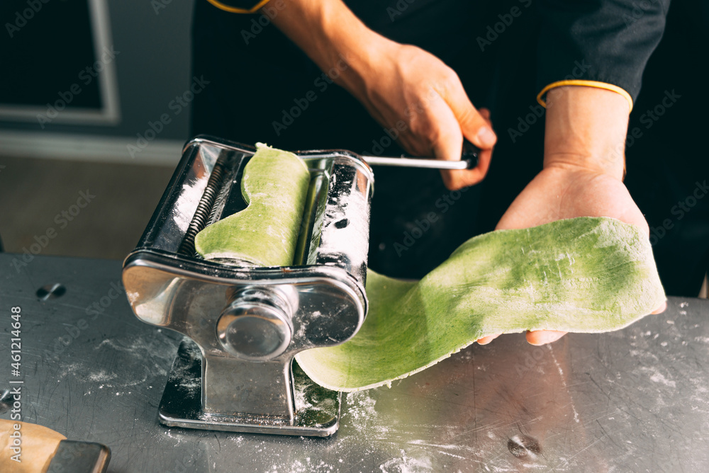 Woman is using pasta making machine for some green pasta dough.