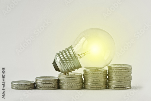 Electric light bulb on raising piles of coins -  Concept of increase in electricity bills