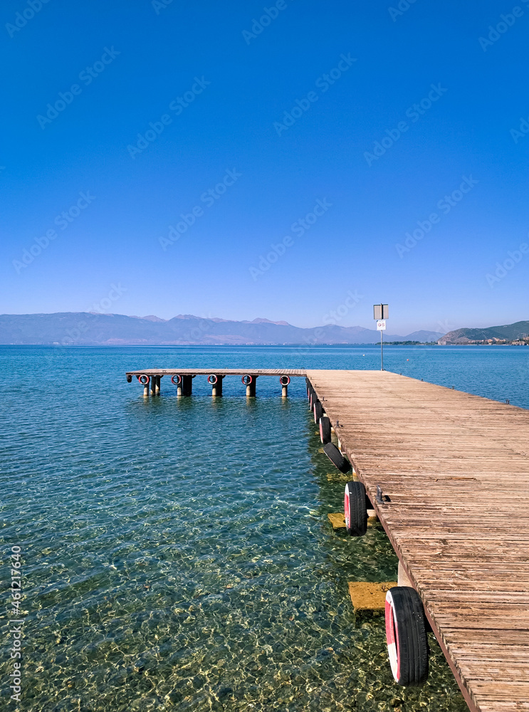 Empty wooden pier on the lake, blue sky, mountains background