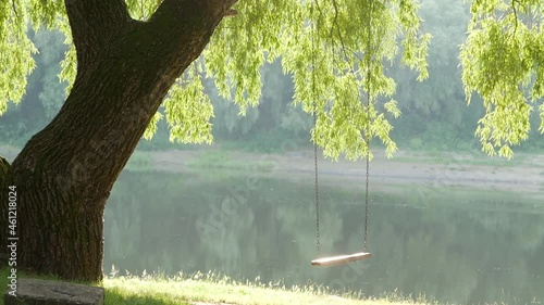 atmospheric video of a swinging swing on the river bank in the setting sun photo