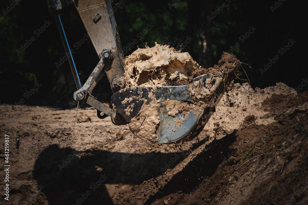 Closeup of a backhoe loader equipment picking scraps and soil from underground by digging ground for construction during a bright and sunny day with water splashing out Closeup of a backhoe loader equipment picking scraps and soil from underground by digging ground for construction during a bright and sunny day with water splashing out