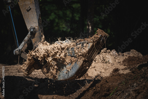 Closeup of a backhoe loader equipment picking scraps and soil from underground by digging ground for construction during a bright and sunny day with water splashing out