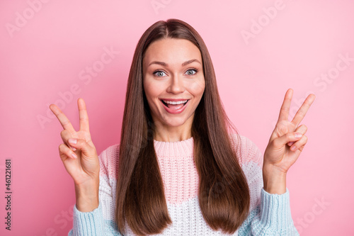 Photo portrait of cheerful model with brunette hair showing v-sign victory both hands smiling isolated on pastel pink color background
